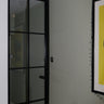 Black framed hinged glass door in modern room with gray wall, radiator, and yellow framed artwork
