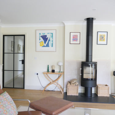 Modern living room with black hinged glass door, wood stove, wicker firewood baskets, and abstract wall art