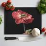 Black chopping board with red poppy print surrounded by cherry tomatoes, basil, garlic, and chef knife