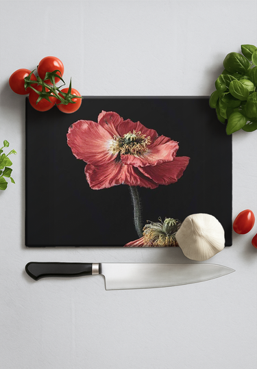 Black chopping board with red poppy print surrounded by cherry tomatoes, basil, garlic, and chef knife