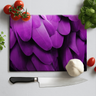 Cutting board with close-up image of purple macaw feathers, surrounded by tomatoes, garlic, and herbs with a kitchen knife
