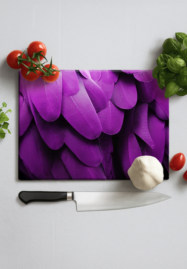 Cutting board with close-up image of purple macaw feathers, surrounded by tomatoes, garlic, and herbs with a kitchen knife