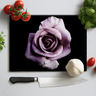 Black chopping board with a large purple rose print, surrounded by cherry tomatoes, garlic, basil, and a kitchen knife