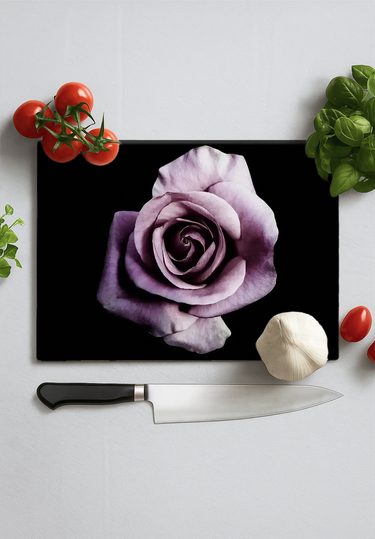 Black chopping board with a large purple rose print, surrounded by cherry tomatoes, garlic, basil, and a kitchen knife