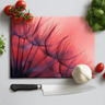 Red dandelion printed glass chopping board with knife, garlic, cherry tomatoes, and basil leaves