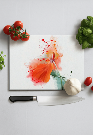 Glass chopping board with a red flower illustration, surrounded by tomatoes, garlic, basil, and a kitchen knife