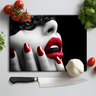 Cutting board with image of woman wearing black lace mask, red lips and nails, surrounded by knife, cherry tomatoes, garlic, and herbs