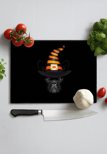 Black chopping board with a black pug wearing an orange and black striped witch hat, surrounded by kitchen items