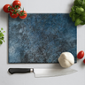 Textured blue chopping board with a chef knife, garlic bulb, fresh tomatoes and basil leaves on white surface