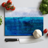 Rectangular chopping board with textured blue shades design surrounded by kitchen knife, garlic, tomatoes, and basil leaves