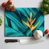 Tropical leaf design cutting board with yellow bird of paradise flower, garlic, tomatoes, basil, and chef knife