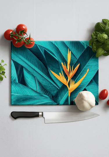 Tropical leaf design cutting board with yellow bird of paradise flower, garlic, tomatoes, basil, and chef knife