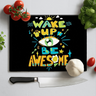 Black chopping board with colorful text 'Wake Up Be Awesome' surrounded by tomatoes, garlic, basil, and a kitchen knife