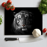 Black chopping board with white tiger face in spotlight surrounded by garlic, cherry tomatoes, basil, and kitchen knife