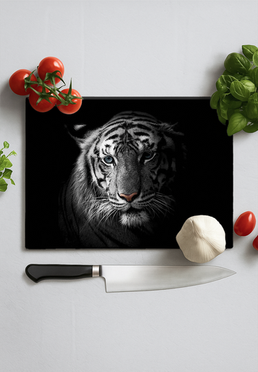 Black chopping board with white tiger face in spotlight surrounded by garlic, cherry tomatoes, basil, and kitchen knife