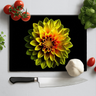 Black chopping board with vibrant yellow and red dahlia print surrounded by cherry tomatoes, garlic, basil, and chef knife