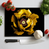 Black chopping board with large yellow peony flower print, surrounded by cherry tomatoes, garlic, basil, and a chef's knife