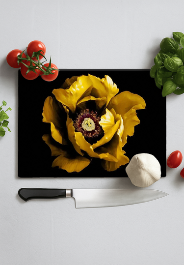 Black chopping board with large yellow peony flower print, surrounded by cherry tomatoes, garlic, basil, and a chef's knife