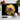 Black chopping board with yellow and purple dahlia design, kitchen knife, garlic, tomatoes, and herbs