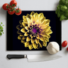 Black chopping board with yellow and purple dahlia design, kitchen knife, garlic, tomatoes, and herbs