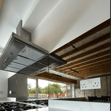 Bespoke mirrored glass splashback in modern kitchen with exposed wooden beams and stainless steel hood