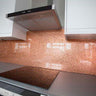 Copper textured glass backsplash in modern kitchen with sleek white cabinets and stainless steel hood
