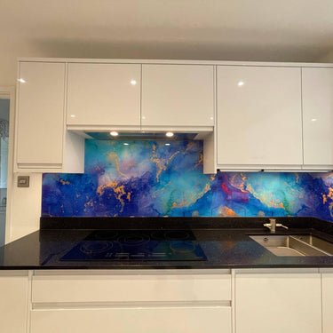 Vibrant blue and gold abstract glass splashback in modern kitchen with white cabinets and black countertop
