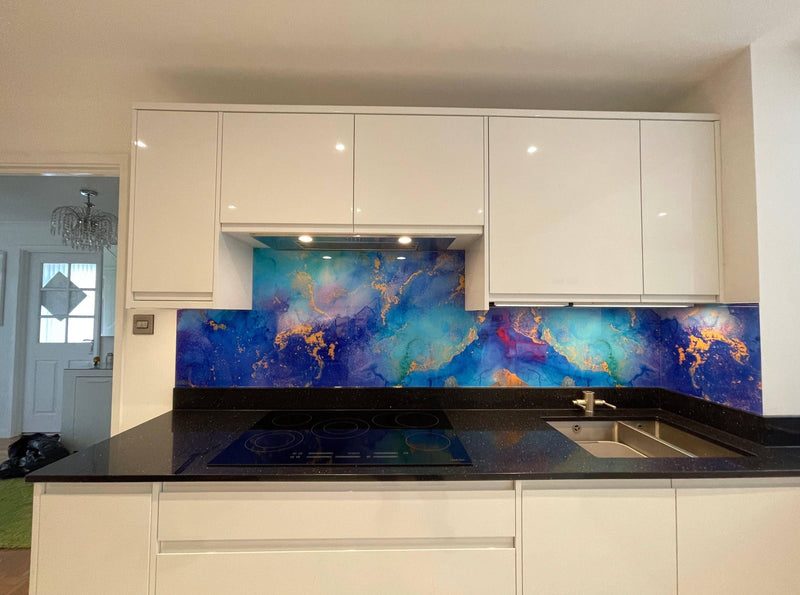 Vibrant blue and gold abstract glass splashback in modern kitchen with white cabinets and black countertop