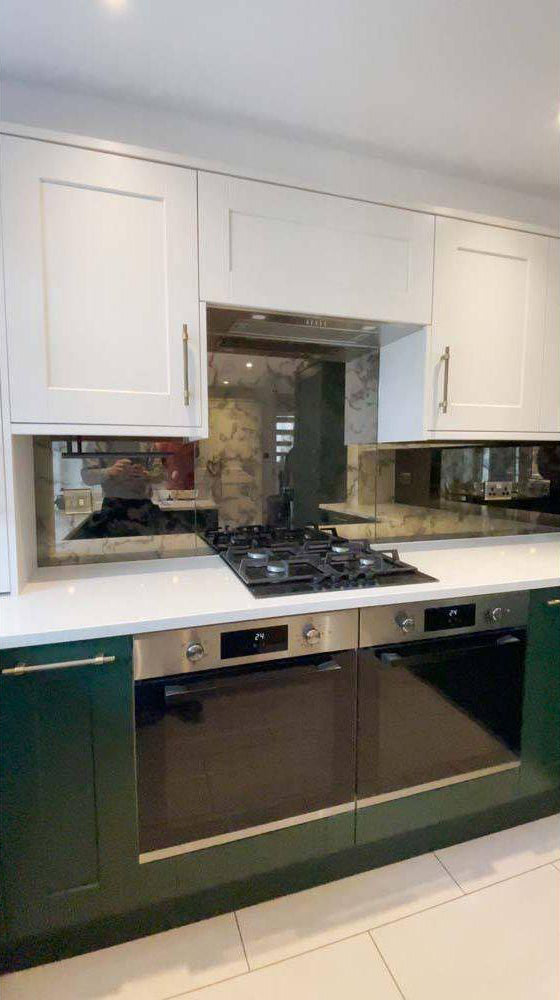 Modern kitchen with custom glass splashback, white cabinets, and green base units