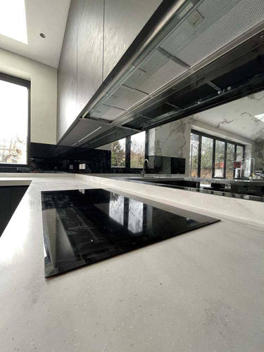 Modern kitchen with sleek black glass cooktop and marble countertops, featuring luxury architectural glass design
