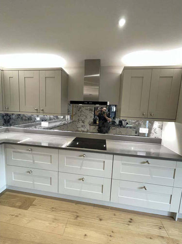 Modern kitchen with sleek white cabinets, marble backsplash, and reflective glass feature wall