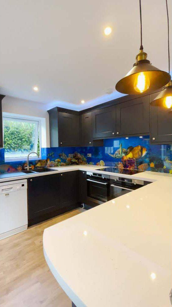 Vibrant underwater scene on custom glass kitchen backsplash with dark cabinets and pendant lights