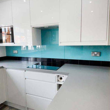 Modern kitchen with turquoise glass splashback, white cabinets, and grey countertop