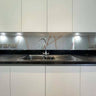 Modern kitchen with sleek white cabinets, black countertop, and decorative glass backsplash featuring red veining.