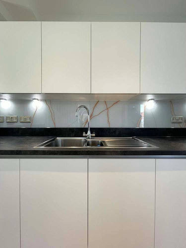 Modern kitchen with sleek white cabinets, black countertop, and decorative glass backsplash featuring red veining.