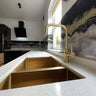 Luxury kitchen with gold sink, brass faucet, and decorative glass backsplash featuring marble patterns.