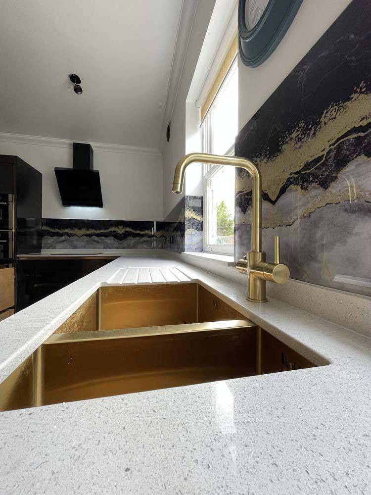 Luxury kitchen with gold sink, brass faucet, and decorative glass backsplash featuring marble patterns.