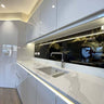 Modern kitchen with LED backlit glass splashback and marble countertop, featuring sleek white cabinetry and under-cabinet lighting.