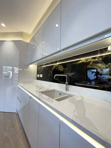 Modern kitchen with LED backlit glass splashback and marble countertop, featuring sleek white cabinetry and under-cabinet lighting.