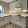Modern kitchen with white shaker cabinets, marble-effect glass backsplash, and under-cabinet lighting