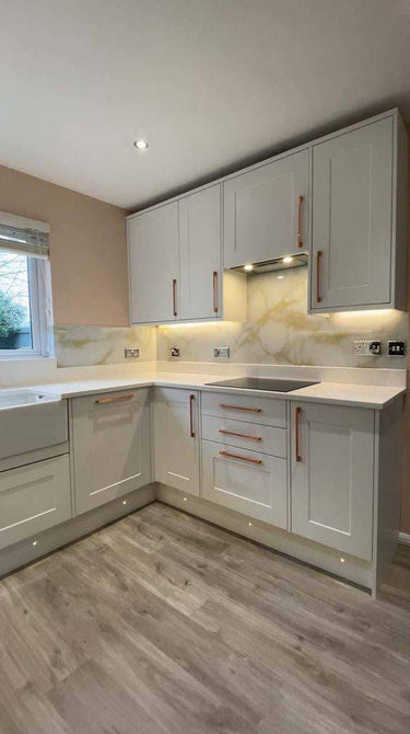 Modern kitchen with white shaker cabinets, marble-effect glass backsplash, and under-cabinet lighting