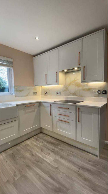 Modern kitchen with white shaker cabinets, marble-effect glass backsplash, and under-cabinet lighting