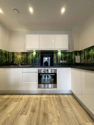 Modern kitchen with forest-print glass splashback, white cabinets, and wood flooring