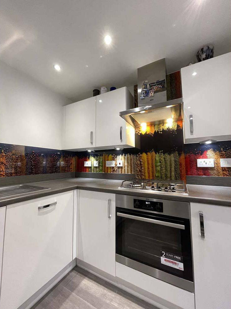 Modern kitchen with colorful decorative glass splashback behind stainless steel hob and oven