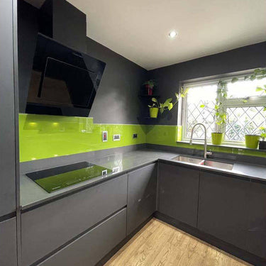 Vibrant lime green glass splashback in modern kitchen with grey cabinets and wooden flooring