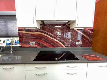 Bespoke red marble-effect glass kitchen splashback with modern white cabinets and black countertop