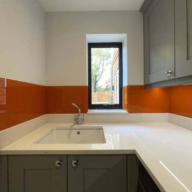 Vibrant orange glass backsplash in modern kitchen with grey cabinets and white countertop