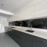 Modern kitchen with sleek black glass splashback and white cabinetry, featuring integrated lighting and minimalist design.