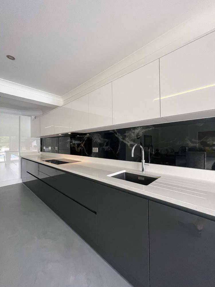 Modern kitchen with sleek black glass splashback and white cabinetry, featuring integrated lighting and minimalist design.