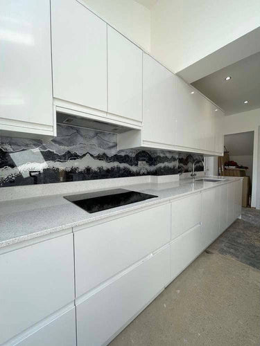 Modern kitchen with bespoke glass splashback featuring mountain wave design, sleek white cabinets, and granite countertop.